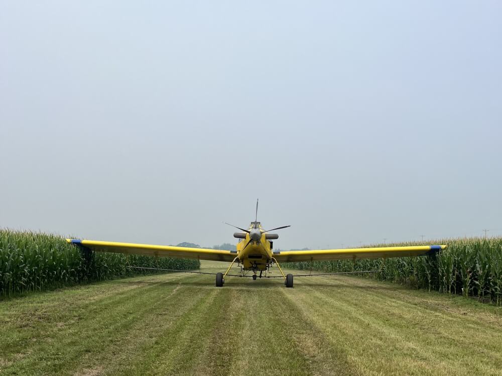 yellow air tractor parked between cornfields